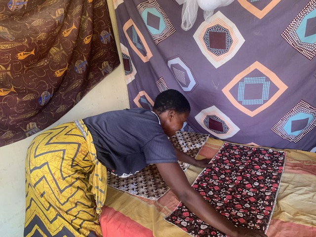 Kazolo's sister in law organising Kazolo's bed with mattress__ protectors.