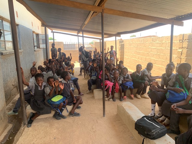 Pupils seated in the shade ready for their midday meal.